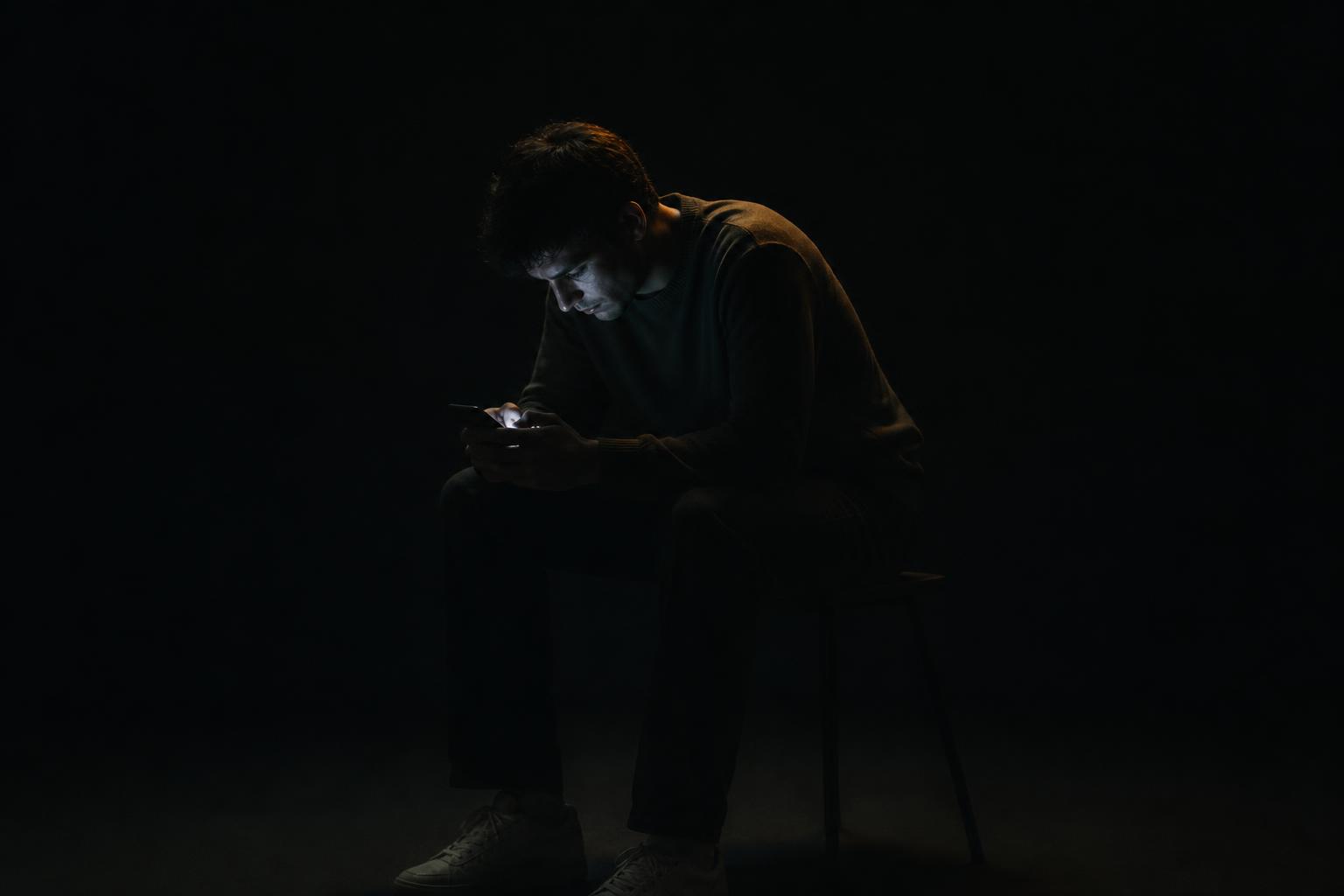 A person sitting alone in the dark, lit only by their phone